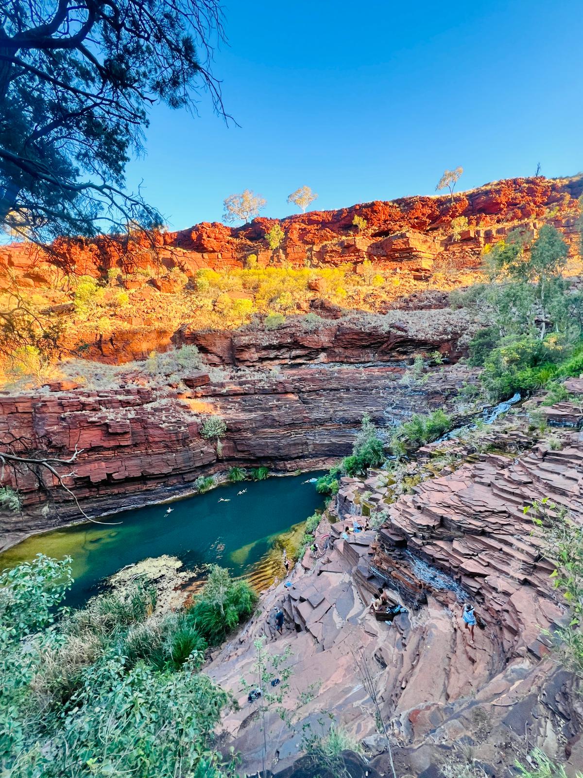 Women swimming in a deep gorge pool beneath a stepped waterfall in Karijini